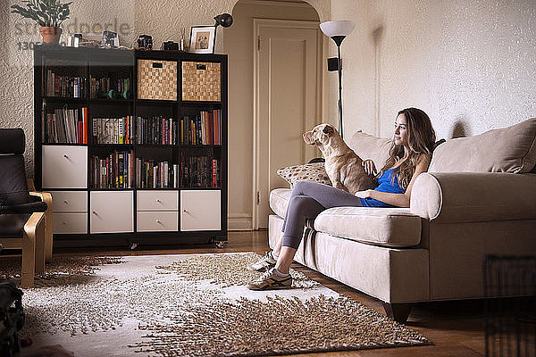 Frau sitzt zu Hause mit Hund auf dem Sofa