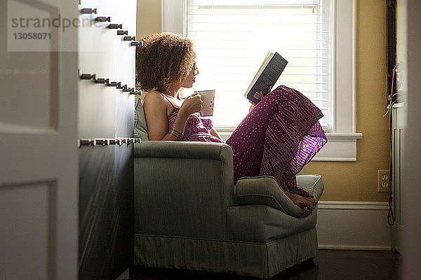 Seitenansicht einer Frau  die ein Buch hält  während sie auf einem Sessel sitzt