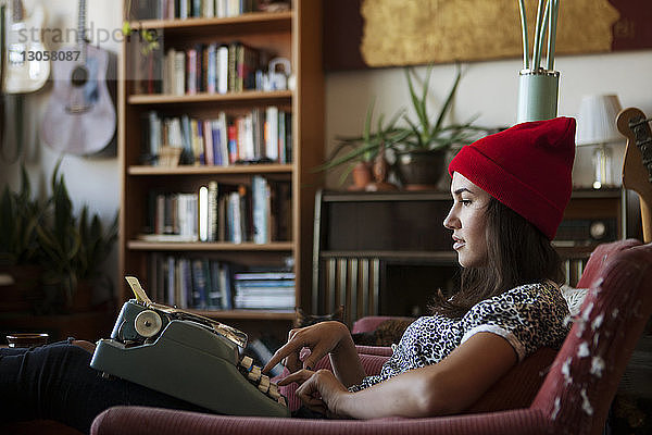 Seitenansicht einer Frau  die eine Schreibmaschine benutzt  während sie auf einem Stuhl sitzt