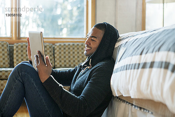 Glücklicher Mann benutzt Tablet-Computer  während er zu Hause am Bett sitzt