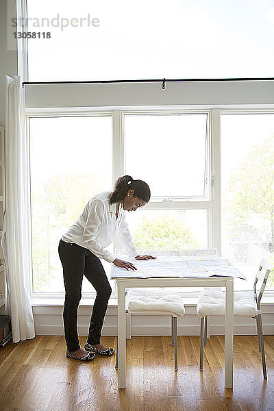 Geschäftsfrau liest Karte am Tisch gegen Fenster im Kreativbüro