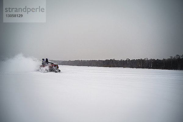 Freunde fahren im Winter Schneemobil auf dem Feld