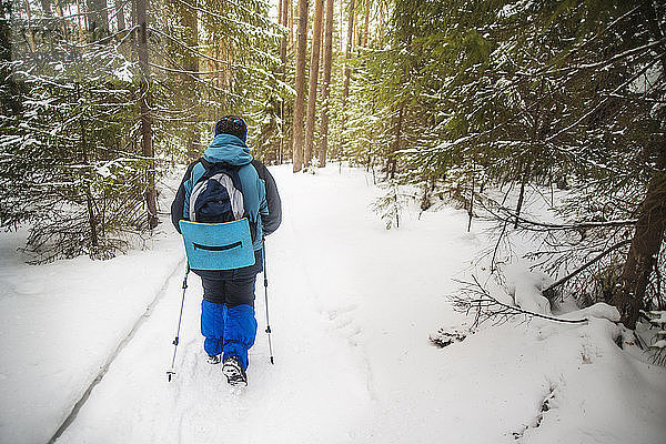 Rückansicht eines Wanderers mit Rucksack beim Wandern im verschneiten Wald