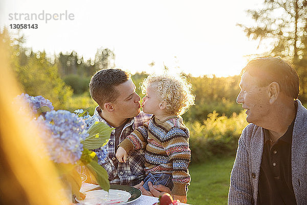Vater küsst Sohn an sonnigem Tag am Picknicktisch