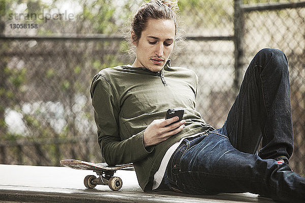 Mann benutzt Mobiltelefon  während er auf einem Sitz im Skateboard-Park sitzt