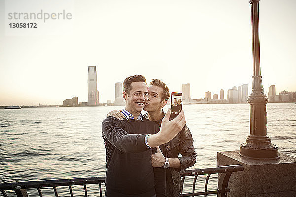 Homosexuelles Paar  das sich am Fluss stehend am Handy selbstständig macht