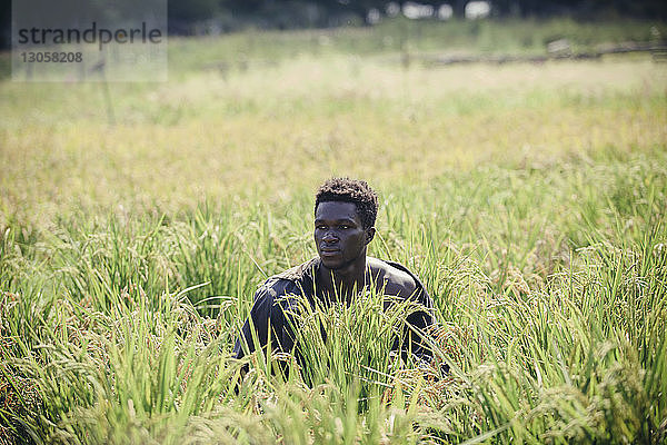 Nachdenklicher Landwirt sitzt inmitten von Pflanzen auf dem Feld
