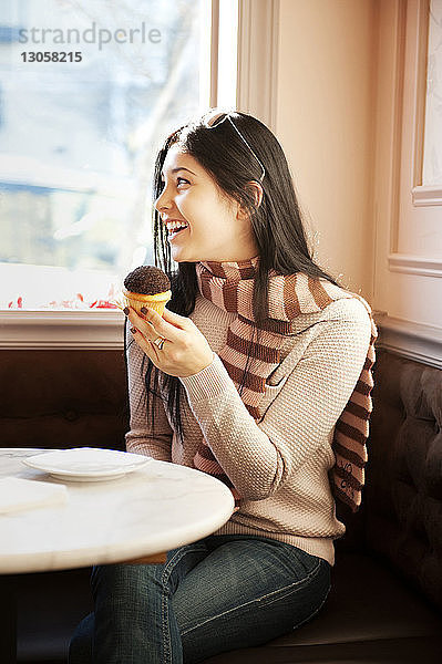 Glückliche Frau hält Muffin  während sie im Restaurant sitzt