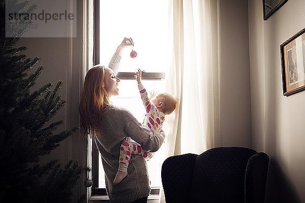 Frau spielt mit kleinem Mädchen  während sie zu Hause am Fenster steht