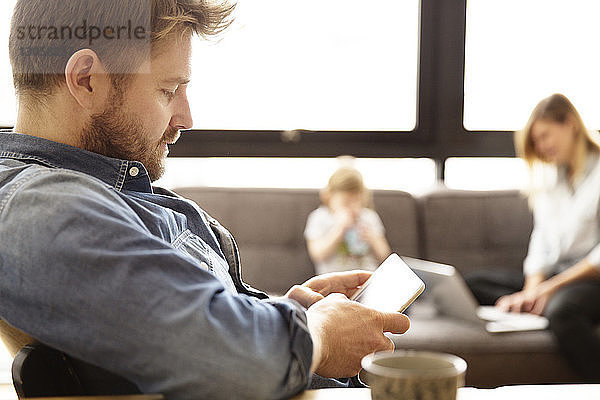 Mann mit Tablet-Computer mit Familie im Hintergrund