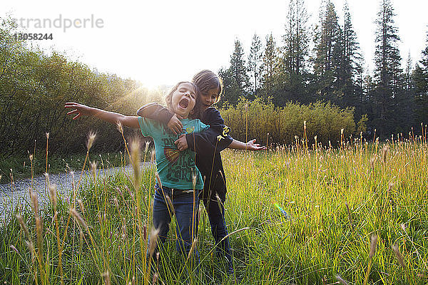Mädchen umarmt Freundin  während sie auf Gras gegen den Himmel steht