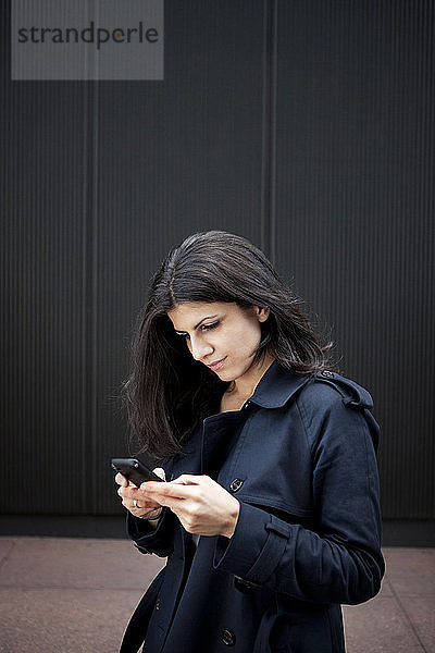 Junge Frau benutzt Smartphone  während sie an der Wand steht
