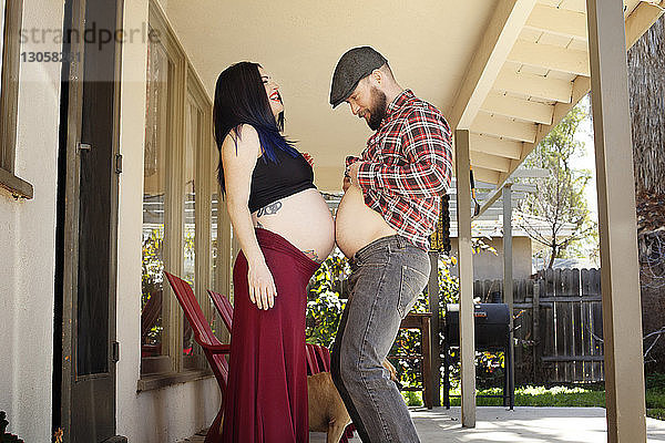 Seitenansicht eines Mannes  der auf der Veranda den Bauch einer schwangeren Frau berührt