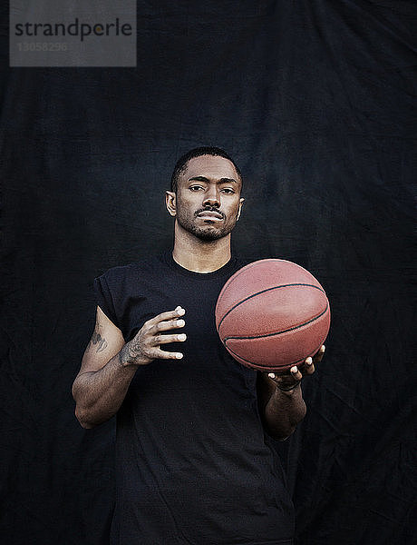 Porträt eines Mannes  der einen Basketball hält  während er an einer schwarzen Wand steht