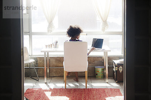 Rückansicht einer Frau  die einen Laptop-Computer benutzt  während sie zu Hause auf einem Stuhl sitzt