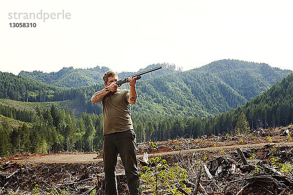 Jäger  der mit dem Gewehr zielt  während er gegen den klaren Himmel steht