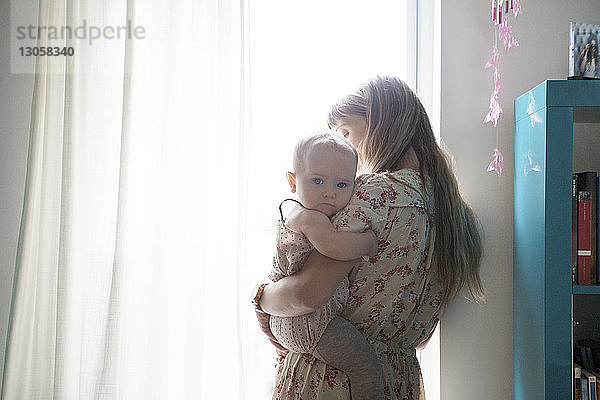 Mutter trägt Baby  während sie am Fenster steht