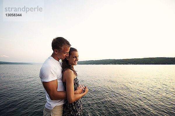 Romantisches Paar steht am See vor klarem Himmel