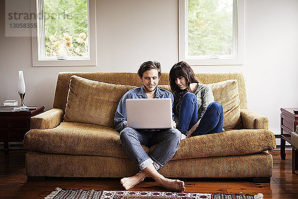 Mann benutzt Laptop-Computer  während er mit seiner Freundin zu Hause auf dem Sofa sitzt
