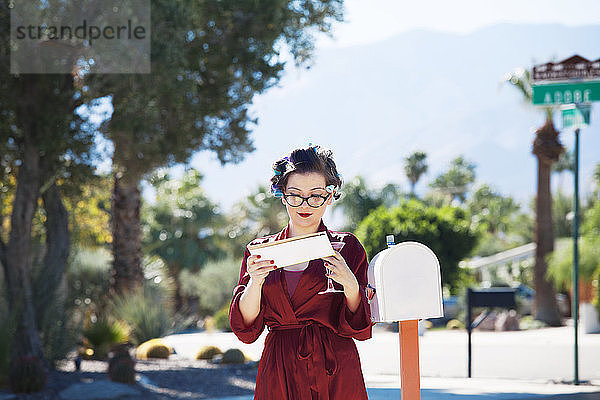 Frau  die Post liest  während sie am Briefkasten steht