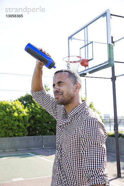 Mann gießt Wasser auf den Kopf  während er im Basketballplatz steht