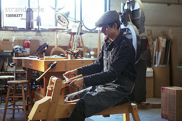 Seitenansicht eines Tischlers  der in der Werkstatt Holz mit dem Ziehmesser rasiert