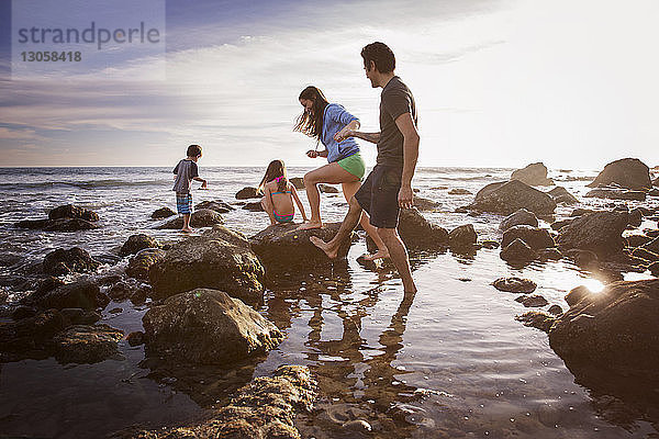 Paar  das beim Spaziergang mit spielenden Kindern am Strand Händchen hält