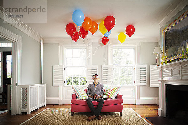 Mann schaut zu Hause auf Luftballons  während er auf dem Sofa sitzt