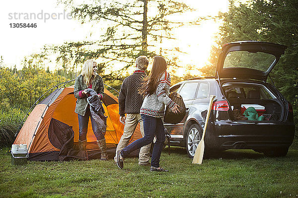 Glückliche Freunde bereiten mit dem Auto auf einem Feld im Wald ein Zelt vor