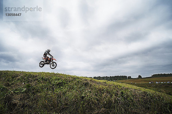 Biker führt Stunt auf Hügel gegen bewölkten Himmel aus