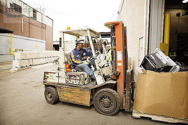Arbeiter bewegt Kiste mit Gabelstapler im Recyclingwerk