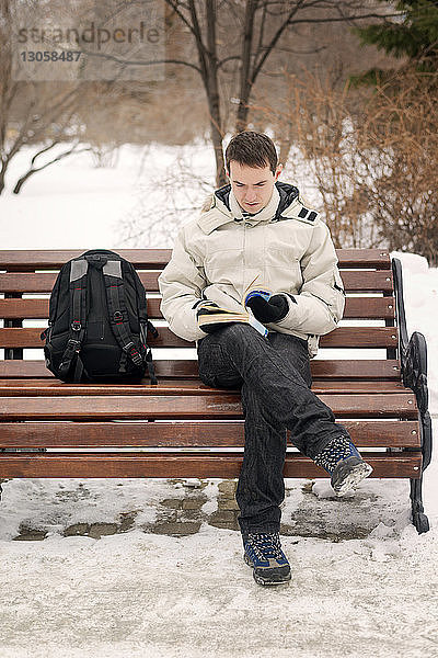Junger Mann liest einen Roman  während er im Winter auf einer Bank sitzt