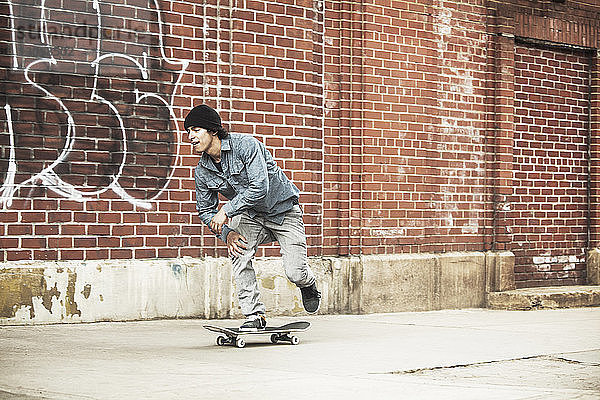 Mann fährt Skateboard auf Fußweg gegen Ziegelmauer