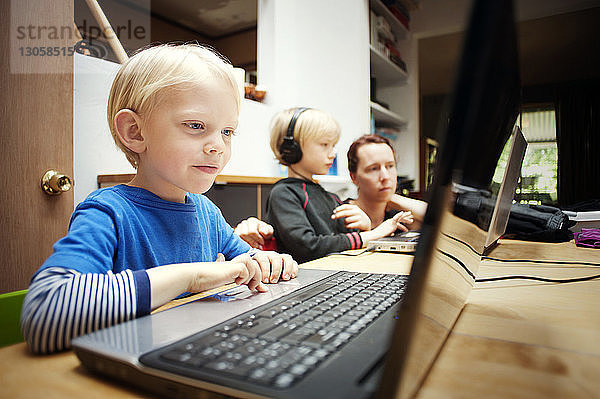 Kinder benutzen Laptop-Computer  während sie bei der Mutter zu Hause sitzen