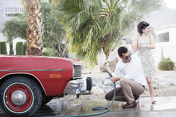 Mann besprüht Frau beim Autowaschen auf Parkplatz mit Wasser