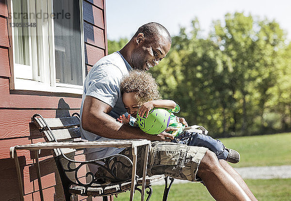 Glückliche Vater und Sohn sitzen mit Ball auf Bank im Hinterhof
