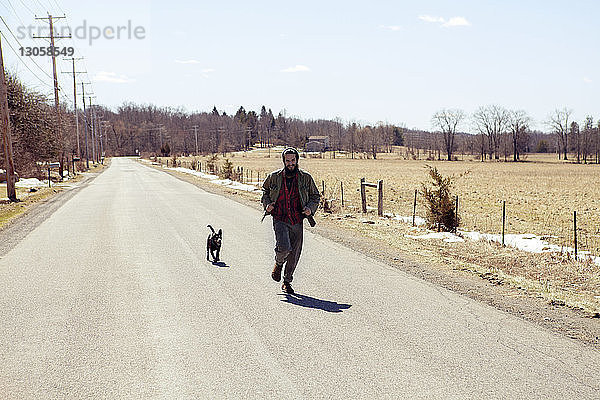 Mann und Hund laufen in voller Länge während des Urlaubs auf der Landstraße