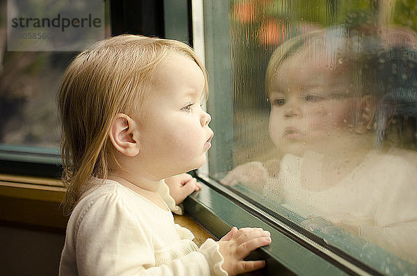 Neugieriges Mädchen schaut durch nasses Fenster