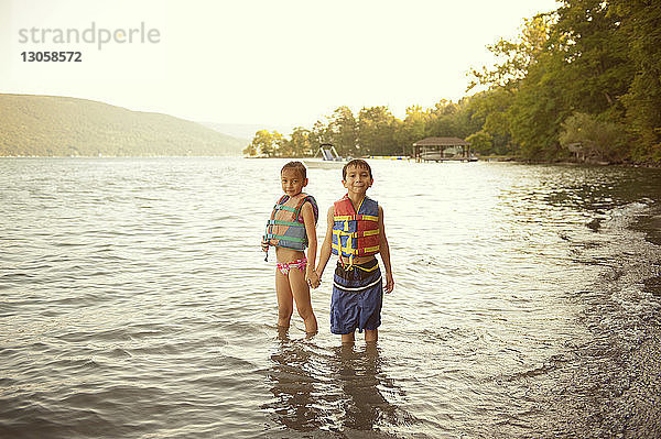 Porträt von Geschwistern in Schwimmwesten  die im See stehen