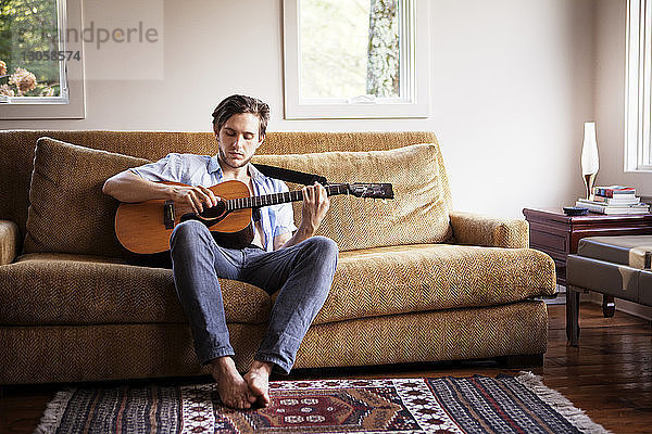 Mann spielt Gitarre  während er auf dem Sofa sitzt