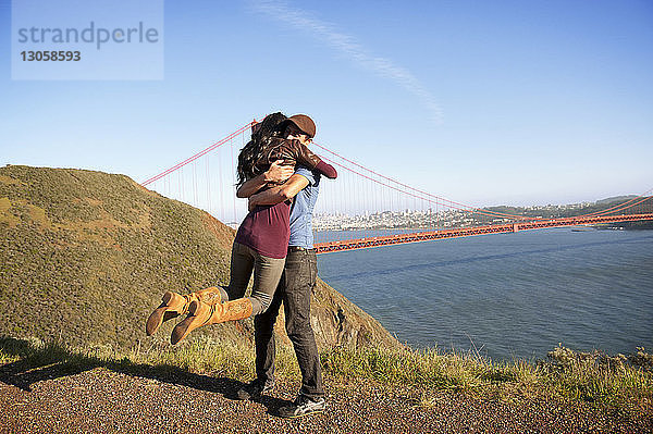 Junges Paar umarmt sich auf dem Spielfeld gegen die Golden Gate Bridge