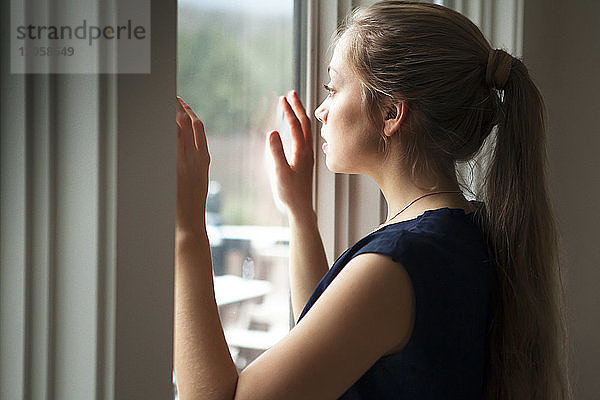 Frau schaut zu Hause durchs Fenster