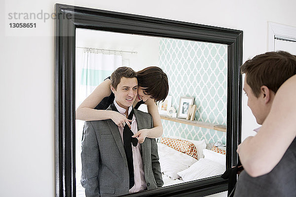 Lächelnde Frau bindet ihrem Freund vor dem Spiegel die Krawatte