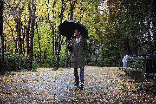 Mann mit Regenschirm geht auf Straße im Park