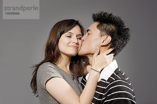 Mann küsst Frau vor grauem Hintergrund