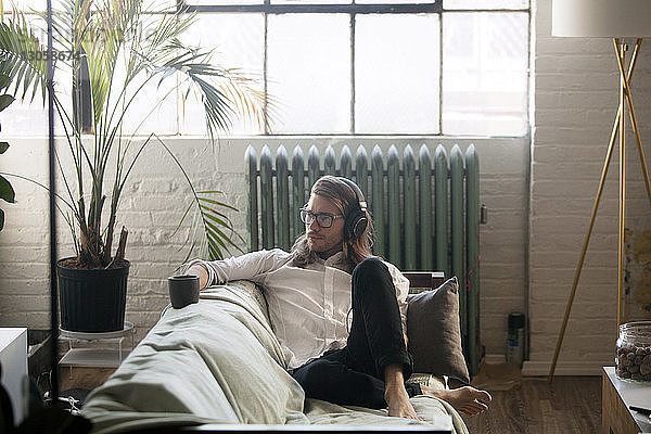Nachdenklicher Mann hört Musik  während er zu Hause auf dem Sofa sitzt