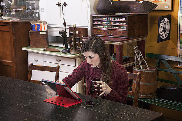 Frau benutzt Tablet-Computer  während sie einen Becher im Bekleidungsgeschäft hält
