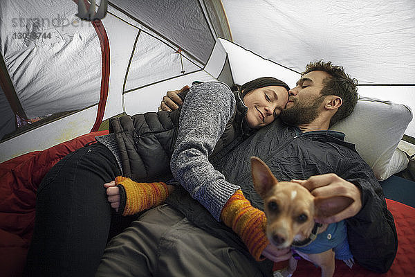 Mann küsst Freundin auf die Stirn  während er sich im Zelt entspannt