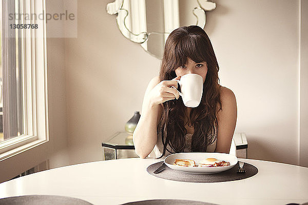 Porträt einer Frau  die zu Hause am Frühstückstisch Kaffee trinkt