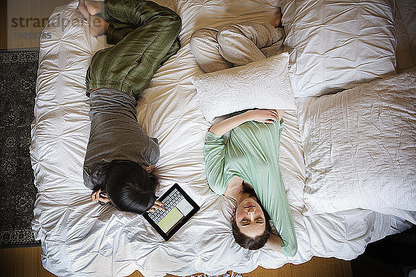 Draufsicht einer Frau  die einen Tablet-Computer benutzt  während sie neben einem Freund zu Hause liegt